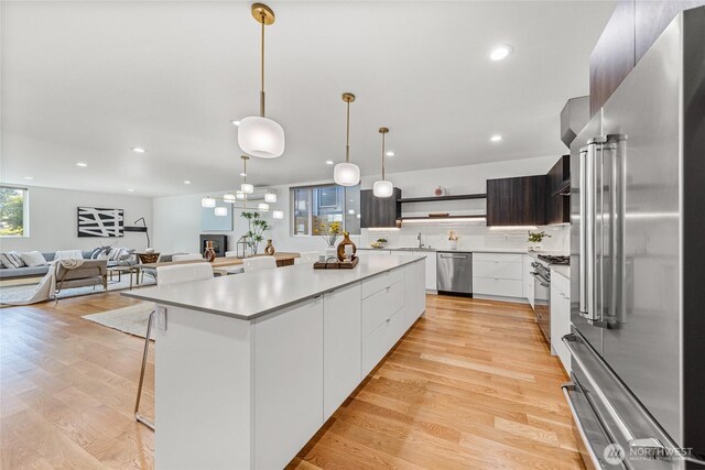 kitchen with open shelves, modern cabinets, a center island, a sink, and appliances with stainless steel finishes