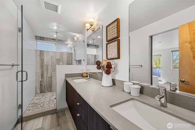 full bathroom with double vanity, a sink, a stall shower, and visible vents