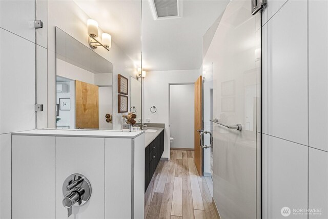 bathroom featuring vanity, toilet, a shower stall, wood finished floors, and visible vents