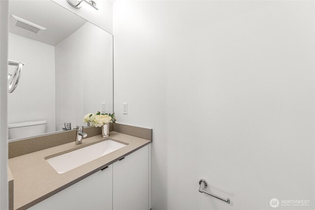 half bathroom featuring toilet, visible vents, and vanity