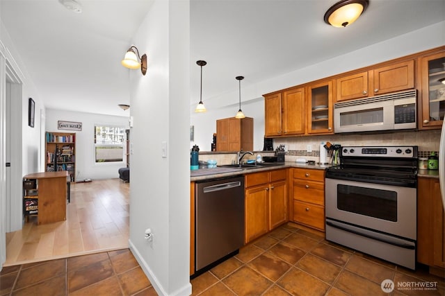 kitchen featuring brown cabinets, dark tile patterned flooring, tasteful backsplash, a sink, and appliances with stainless steel finishes
