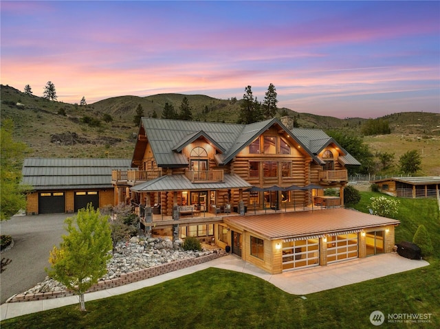 log-style house with a front yard, a mountain view, a chimney, concrete driveway, and a balcony