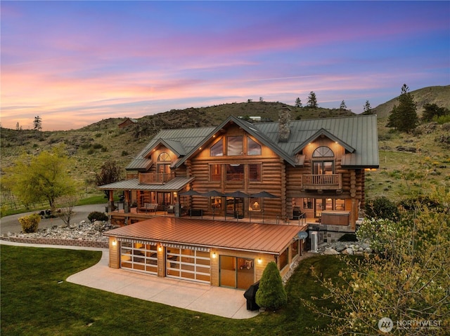 back of house at dusk with a mountain view, a balcony, a chimney, and concrete driveway