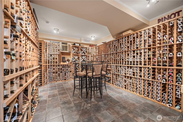 wine cellar with crown molding, an AC wall unit, stone finish flooring, and visible vents