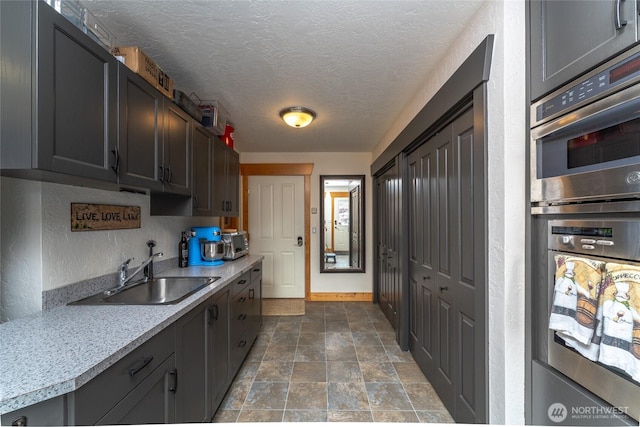 kitchen with a sink, double oven, light countertops, a textured ceiling, and stone finish flooring