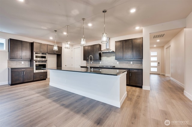 kitchen with visible vents, dark countertops, wall chimney range hood, a sink, and backsplash