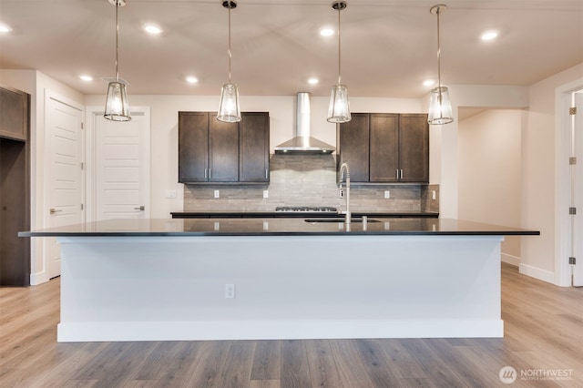 kitchen with dark brown cabinetry, dark countertops, tasteful backsplash, a sink, and wall chimney exhaust hood