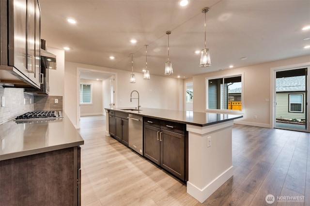 kitchen with dark brown cabinetry, a sink, baseboards, stainless steel appliances, and a wealth of natural light