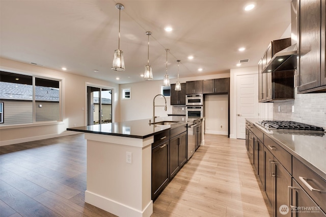 kitchen with dark brown cabinetry, backsplash, appliances with stainless steel finishes, dark countertops, and a sink