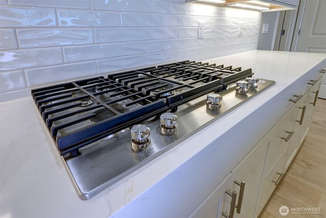 details with light stone counters, light wood finished floors, white cabinetry, decorative backsplash, and stainless steel gas stovetop