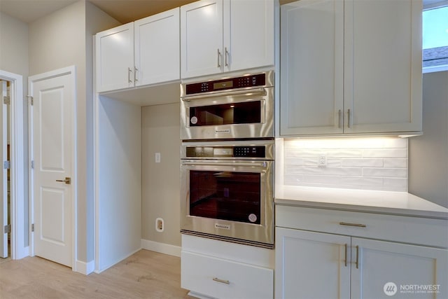 kitchen with double oven, light countertops, light wood-style flooring, and white cabinetry
