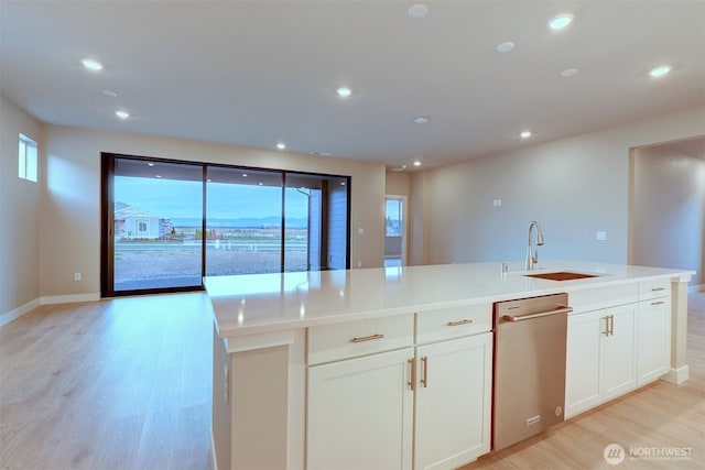 kitchen with a center island with sink, light wood-type flooring, dishwasher, a sink, and white cabinets