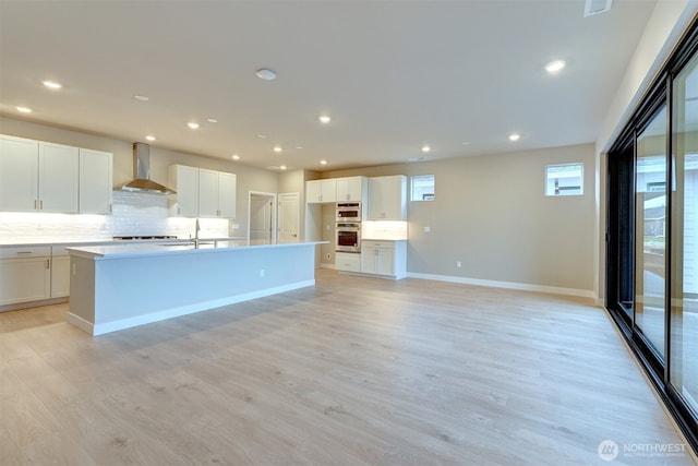 kitchen with wall chimney exhaust hood, white cabinetry, and tasteful backsplash