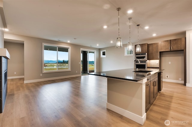 kitchen with baseboards, a kitchen island with sink, light wood-type flooring, and open floor plan