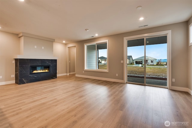 unfurnished living room featuring visible vents, wood finished floors, baseboards, recessed lighting, and a high end fireplace