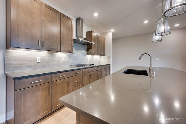 kitchen featuring wall chimney range hood, a sink, stainless steel gas stovetop, tasteful backsplash, and pendant lighting