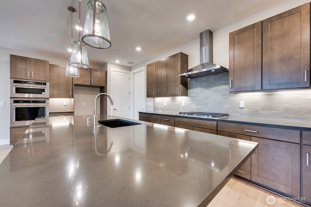 kitchen featuring wall chimney range hood, stainless steel appliances, a sink, and tasteful backsplash