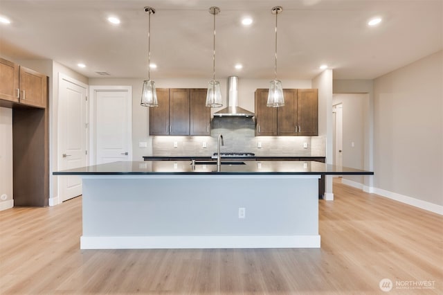 kitchen with wall chimney range hood, dark countertops, tasteful backsplash, and a sink