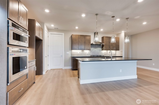 kitchen with pendant lighting, light wood-type flooring, wall chimney exhaust hood, a sink, and backsplash