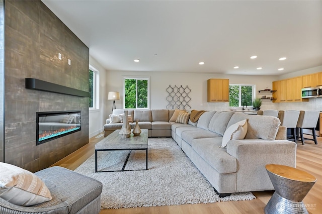 living area with light wood finished floors, recessed lighting, a tiled fireplace, and baseboards