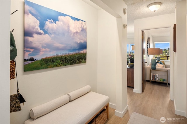 hall with baseboards, light wood finished floors, and a textured ceiling
