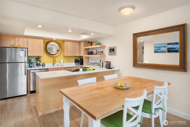 kitchen with a sink, light brown cabinets, light countertops, stainless steel appliances, and light wood-type flooring