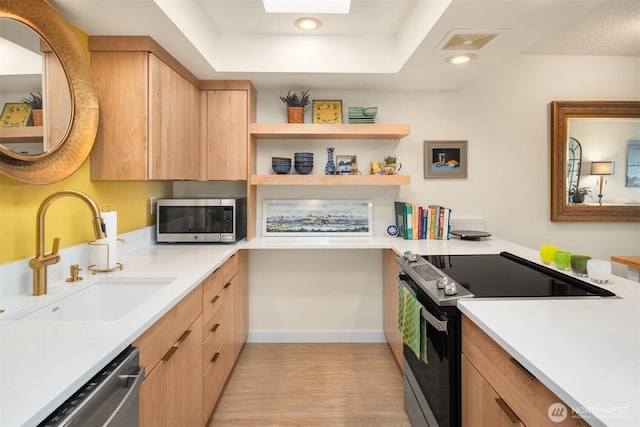 kitchen featuring light brown cabinetry, light wood-style floors, light countertops, a sink, and appliances with stainless steel finishes