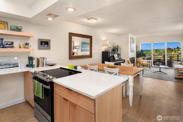 kitchen featuring light brown cabinetry, stainless steel electric range oven, light wood finished floors, a peninsula, and open floor plan