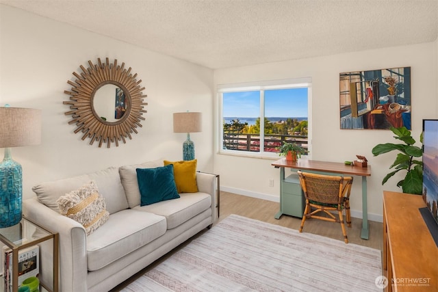 living room with light wood-type flooring, a textured ceiling, and baseboards
