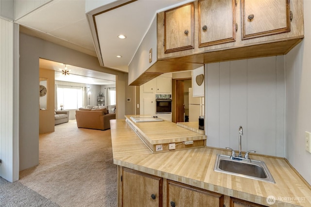 kitchen with a sink, open floor plan, light carpet, recessed lighting, and oven