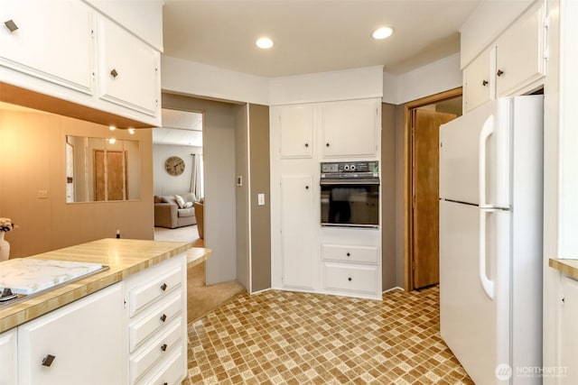 kitchen with freestanding refrigerator, white cabinetry, black oven, and light countertops
