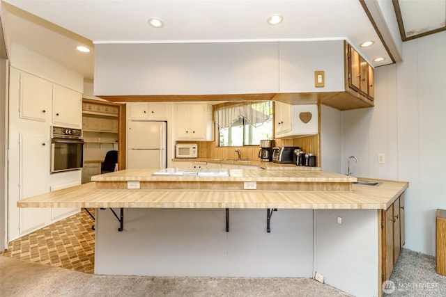 kitchen with a sink, a peninsula, white appliances, and light countertops