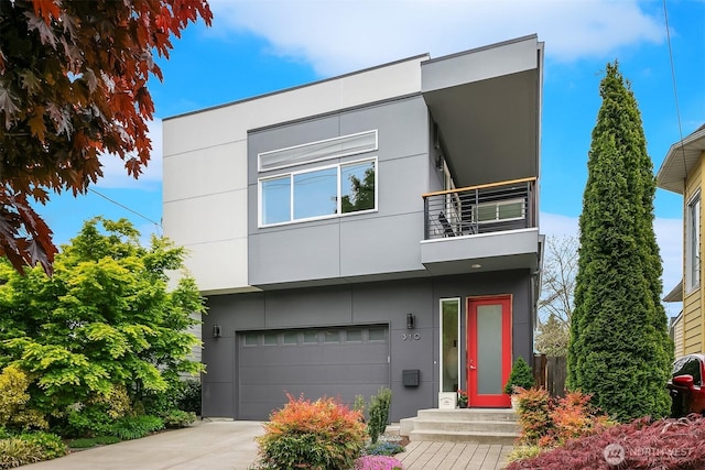 contemporary house with an attached garage, stucco siding, a balcony, and concrete driveway