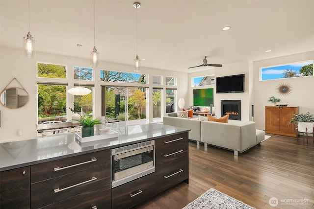 kitchen featuring stainless steel microwave, a glass covered fireplace, dark brown cabinetry, and ceiling fan