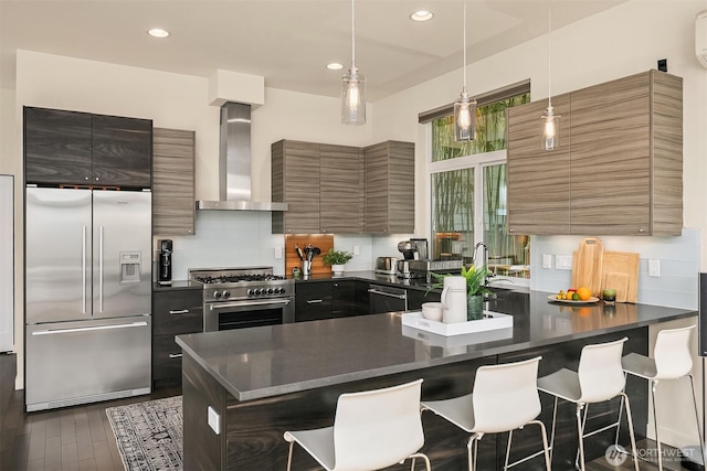 kitchen with wall chimney range hood, high quality appliances, dark countertops, and modern cabinets