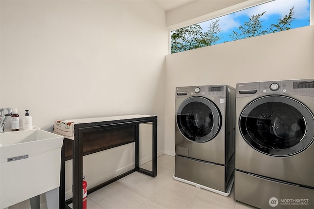 clothes washing area with laundry area, independent washer and dryer, a sink, baseboards, and light tile patterned flooring