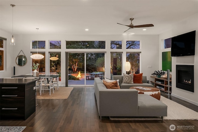 living room featuring dark wood-type flooring, recessed lighting, ceiling fan, and a warm lit fireplace
