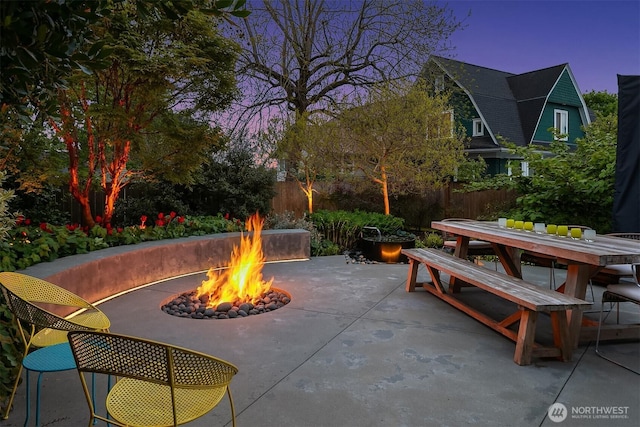 patio terrace at dusk with fence, outdoor dining space, and an outdoor fire pit