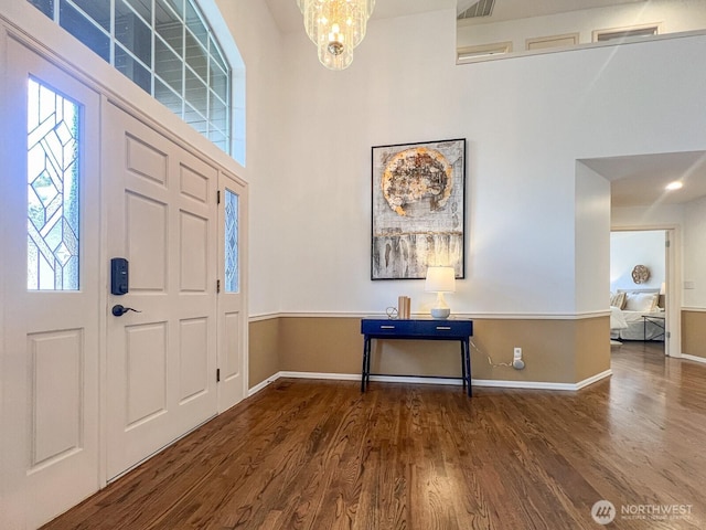 foyer with baseboards, a towering ceiling, wood finished floors, and an inviting chandelier