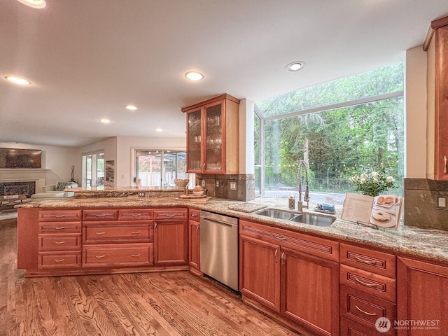 kitchen with stainless steel dishwasher, a peninsula, glass insert cabinets, a sink, and light wood finished floors
