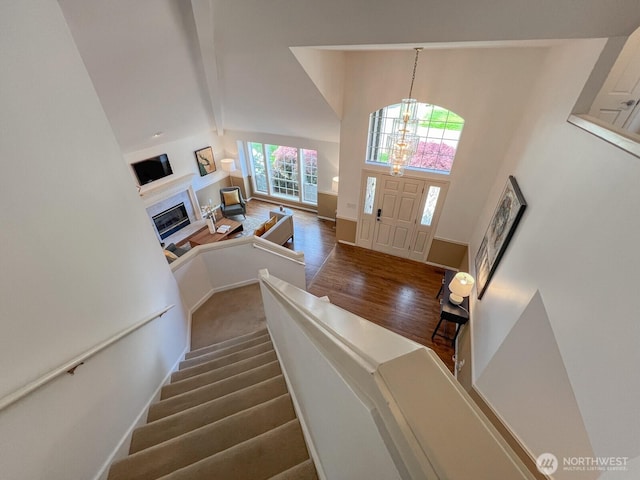 foyer with high vaulted ceiling, a glass covered fireplace, wood finished floors, beamed ceiling, and stairway