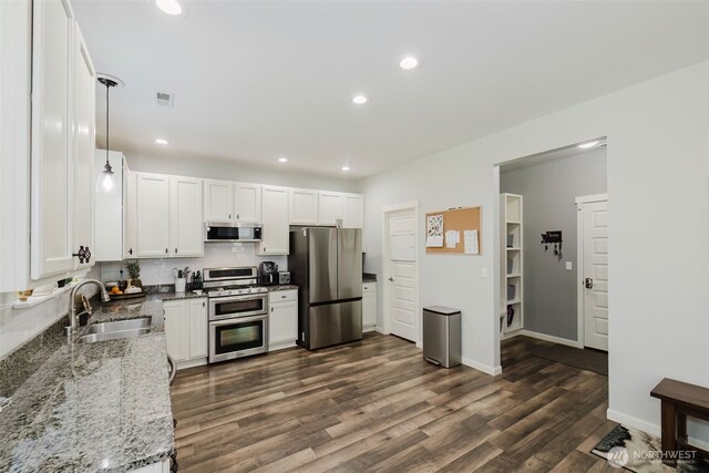 kitchen with appliances with stainless steel finishes, light stone counters, a sink, dark wood finished floors, and white cabinetry