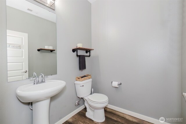half bathroom with visible vents, wood finished floors, toilet, baseboards, and a sink
