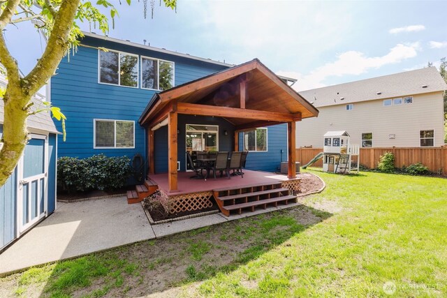 rear view of house with fence, a wooden deck, a playground, a lawn, and outdoor dining space