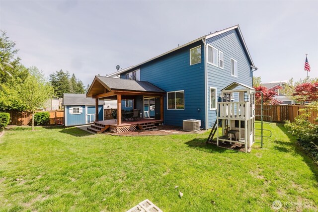 back of house featuring a deck, an outdoor structure, a fenced backyard, a playground, and a shed
