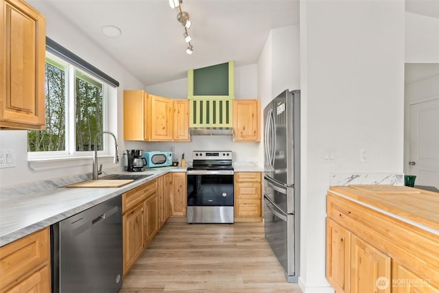 kitchen featuring appliances with stainless steel finishes, light brown cabinetry, a sink, lofted ceiling, and light wood-style floors