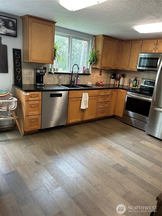kitchen featuring light wood-type flooring, a sink, decorative backsplash, and appliances with stainless steel finishes