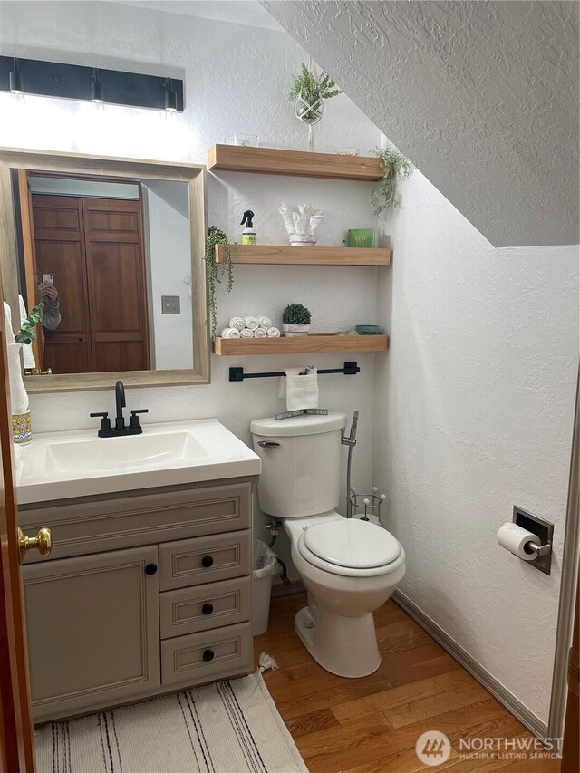 bathroom featuring vanity, a textured wall, wood finished floors, toilet, and baseboards
