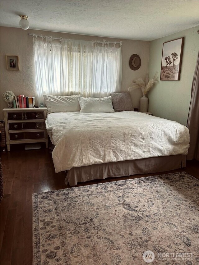 bedroom with a textured wall, dark wood finished floors, and a textured ceiling