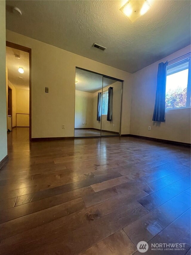 unfurnished room with baseboards, a textured ceiling, visible vents, and hardwood / wood-style floors